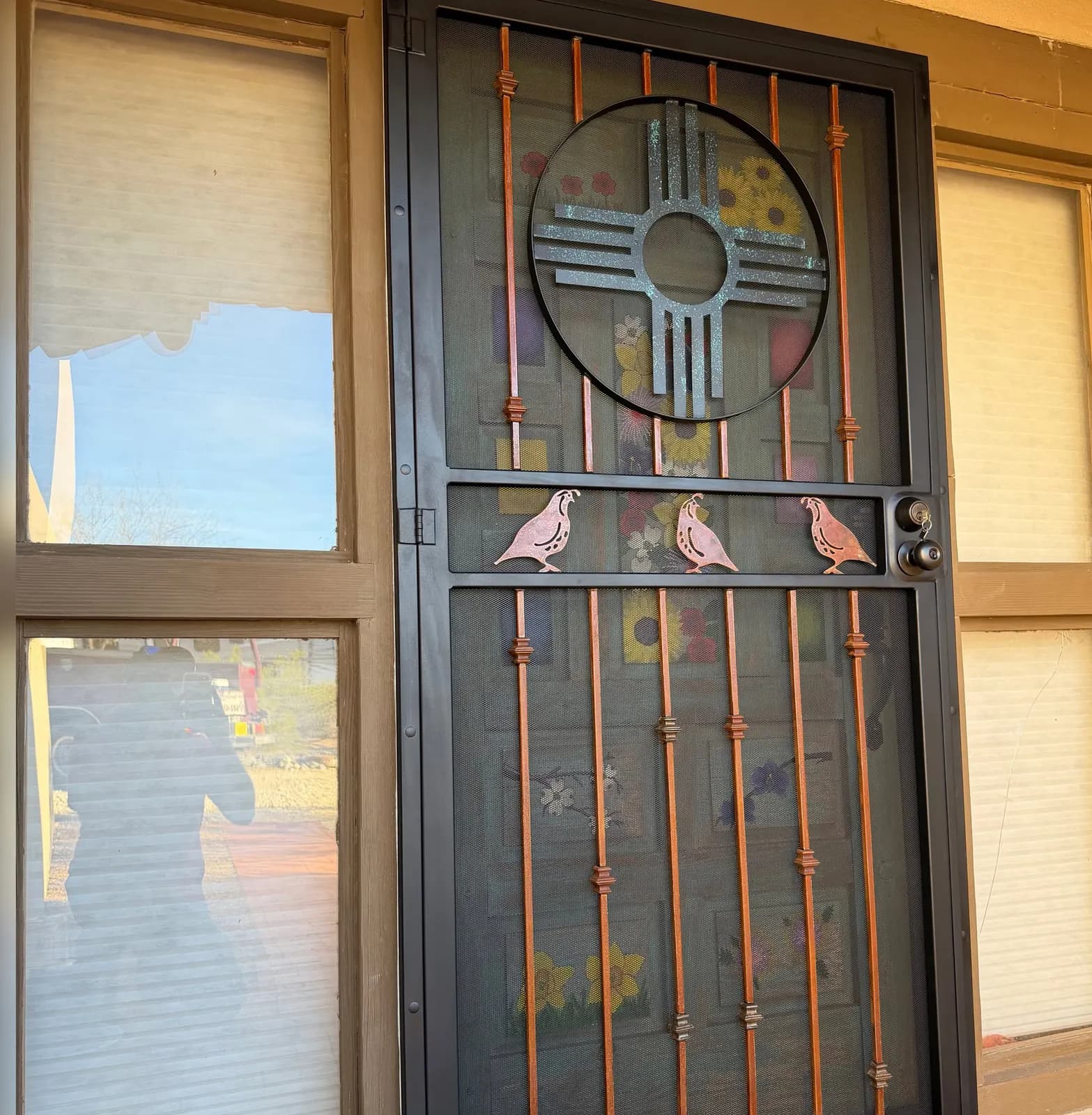 Black security screen door with a Zia sun, quail cutouts, and copper-finish bars on a Las Cruces home